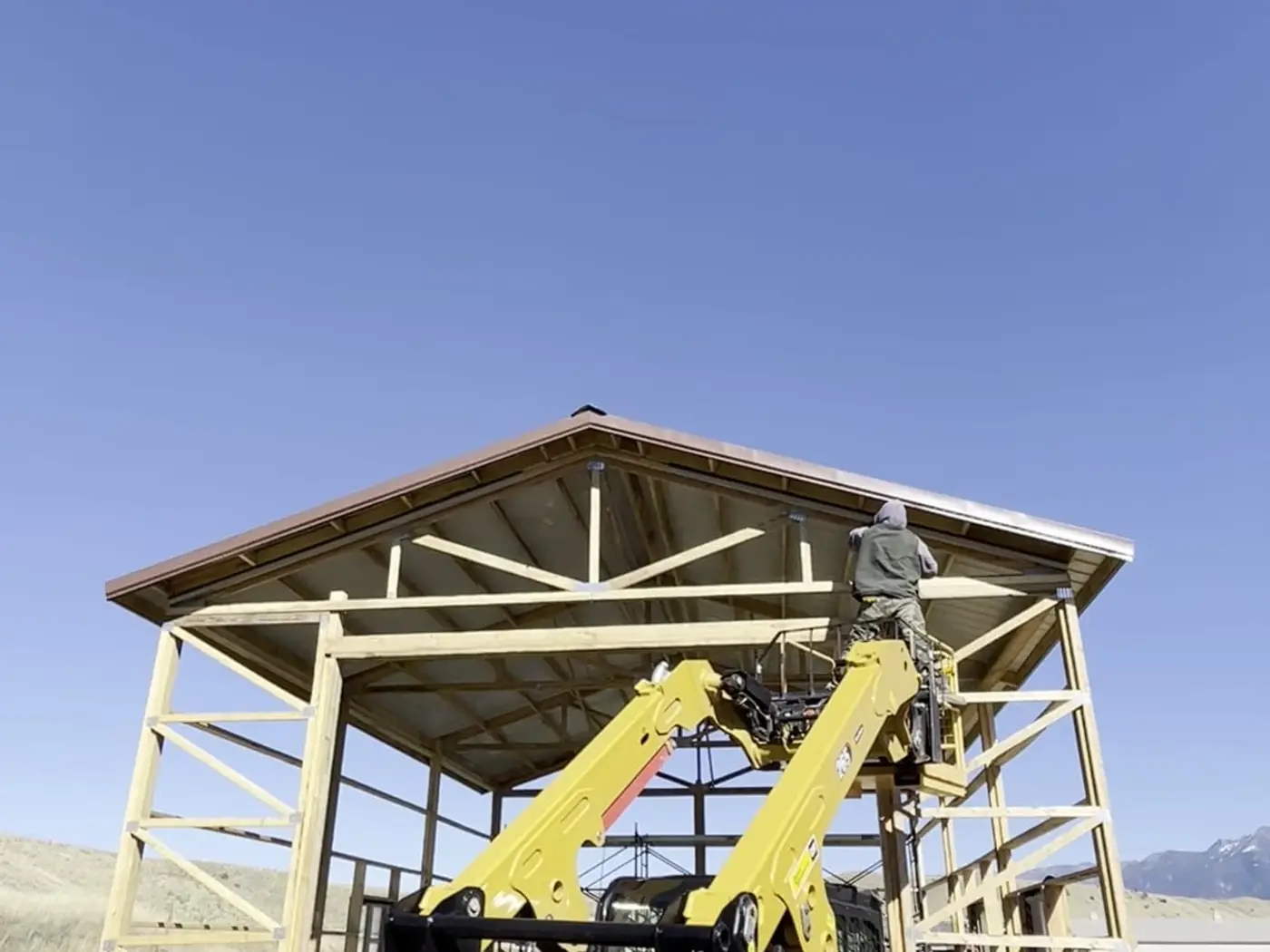 Crew installing roof steel on a pole barn from a lift